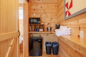 A compact wooden cabin with a kitchenette, including a refrigerator, microwave, and shelves with towels and mugs. - Cabin w/ Sauna in Mid-Coast Maine! Hour to Bar Harbor and Acadia- Cabin #6 Birch (Stockton Springs)
