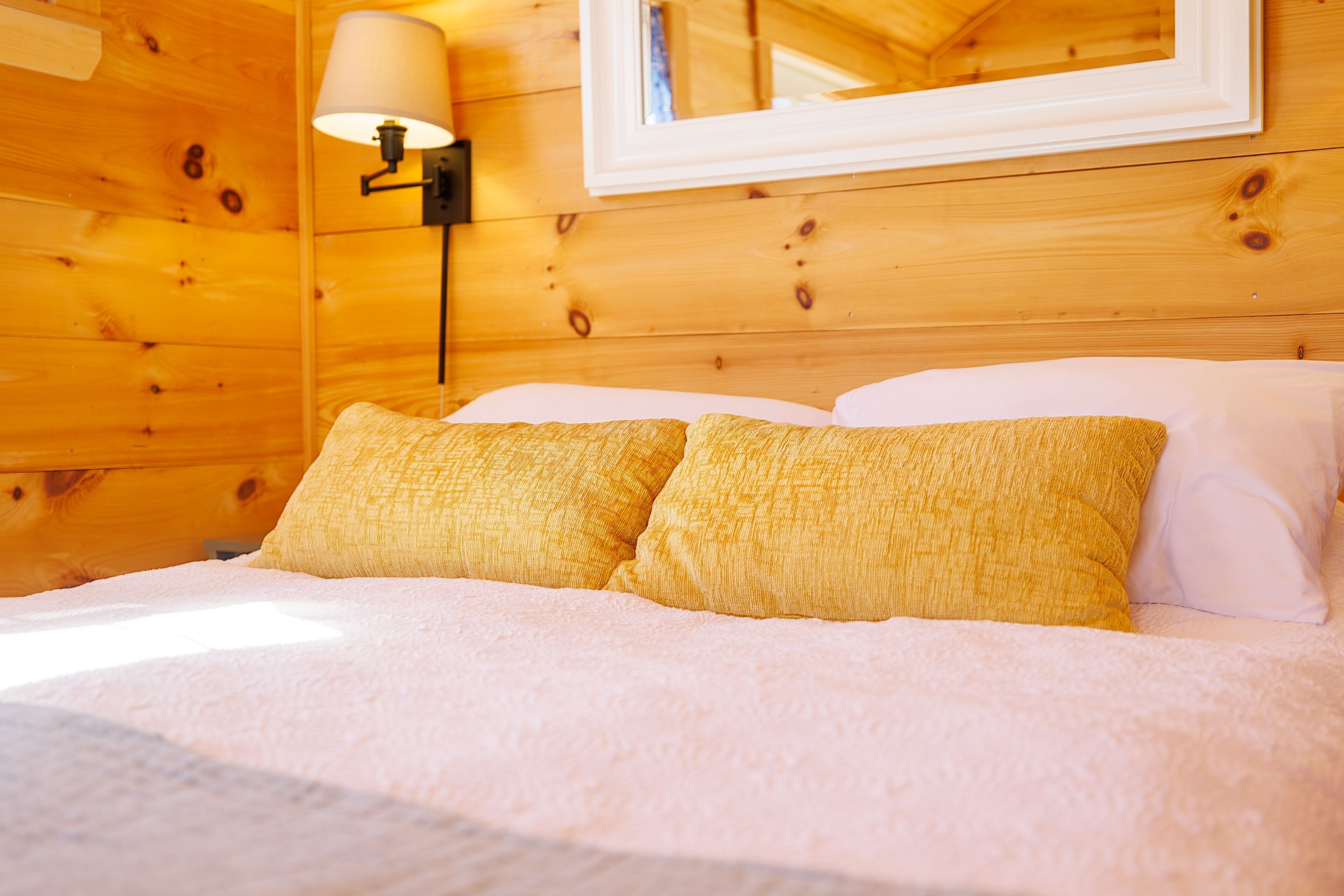 Habitación de cabaña de madera con cama, dos almohadas, mesita de noche y lámpara de pared.