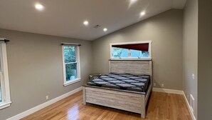 Ein Schlafzimmer mit Holzboden, einem Bett, einem Fenster und einer Deckenleuchte.