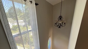 Eine Treppe mit Holzbodenstufen führt zu einer Zwischenebene, eine weiße Wand mit einer dekorativen Leuchte und ein Fenster mit einem gemusterten Vorhang.