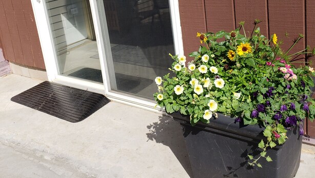 A sliding glass door leading to a patio area with a large planter filled with various flowers. - Rural Somerset Get-A-Way (New Richmond)