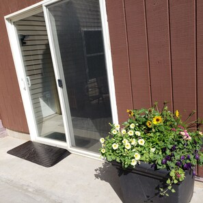 A sliding glass door leading to a patio area with a large planter filled with various flowers.