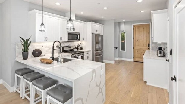 A modern kitchen with white cabinetry, a marble island, and bar stools. - Entire Brand New Luxury Townhouse! #2 (San Diego)