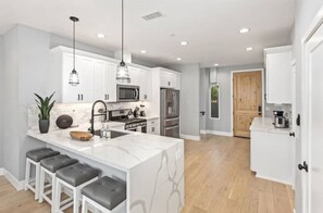 A modern kitchen with white cabinetry, a marble island, and bar stools. - Entire Brand New Luxury Townhouse! #2 (San Diego)