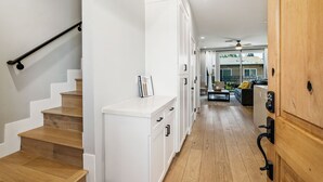 A modern interior with a wooden staircase, white cabinetry, and a view into a living area with a sofa and a dining table. - Entire Brand New 2-Bedroom #5 Luxury Townhouse! (San Diego)