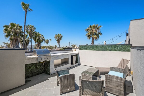 An outdoor patio with a grill, wicker furniture, and palm trees.