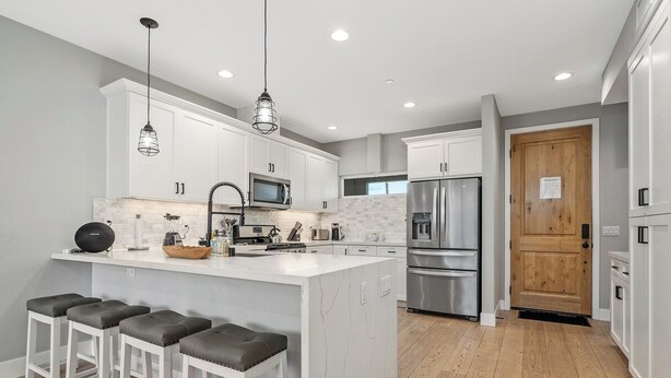 A modern kitchen with white cabinets, a central island with stools, stainless steel appliances, and pendant lighting. - Entire Brand New 2-Bedroom #5 Luxury Townhouse! (San Diego)