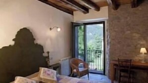 Ein gemütliches Schlafzimmer mit Holzbalkendecke, einem großen Bett mit Quiltdecke, einem Nachttisch und einem Sessel neben einer Schiebetür zu einem Balkon.