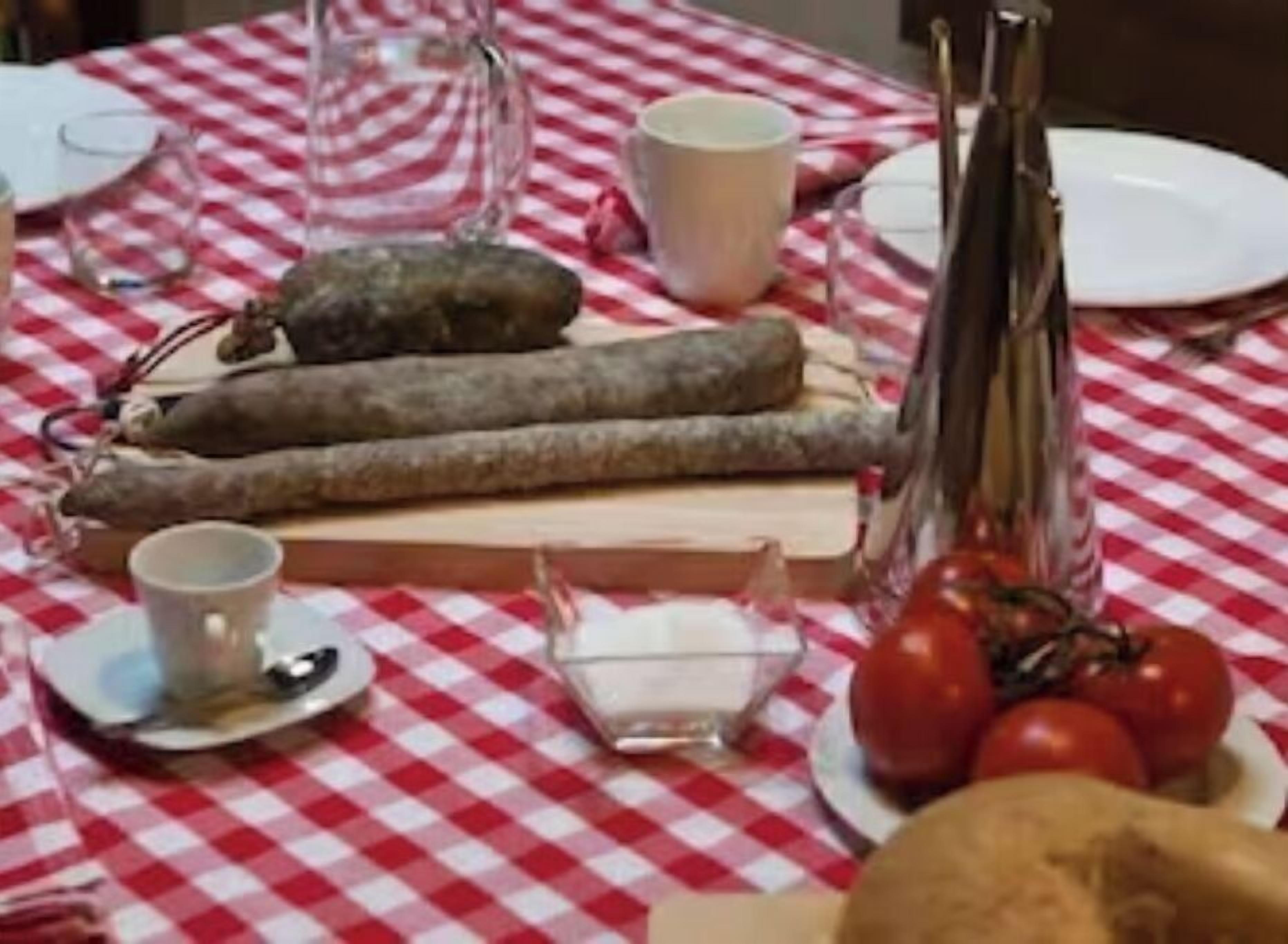 Une table recouverte d’une nappe à carreaux, une assiette avec des tomates, un pain et une bouteille.