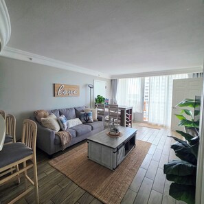 A living room with a grey sofa, a coffee table, and a dining area with chairs and a table.
