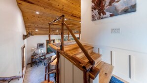 A wooden staircase leading to a loft area with a rustic ceiling, a dining table, and a painting of a cow. - River Run - Luxurious Adults Only Riverfront Oasis (Wimberley)