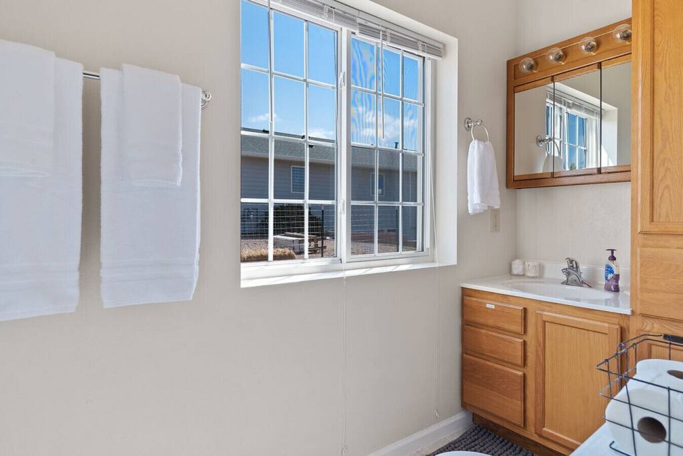 Une salle de bain dotée d’une grande fenêtre, de meubles en bois et d’un miroir avec éclairage intégré.