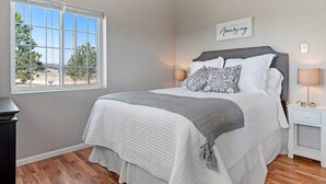 A bedroom with a large window, a bed with patterned pillows, a bedside table with a lamp, and a sign on the wall. - Unique Barn Retreat by the Hills (Rapid City)