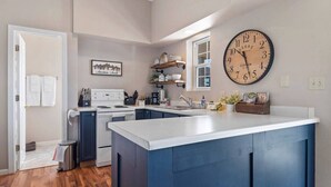 A modern kitchen with a central island, a large wall clock, and a window providing natural light. - Unique Barn Retreat by the Hills (Rapid City)
