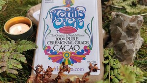 Una confezione di Keit's Cacao, etichettata come cacao cerimoniale puro al 100%, posizionata all'aperto con una candela e elementi naturali.