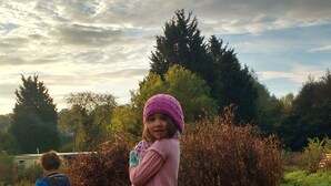 Un bambino in un prato erboso, sullo sfondo alberi e cielo nuvoloso.