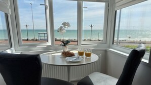 A table with a plant, croissant, and two glasses of orange juice, overlooking a beach. - Beach 180: Beachfront Apartment, Sea views & Private Driveway Parking  (Worthing)