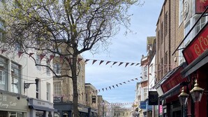 A bustling street with outdoor seating at cafes, a variety of shops, and a tree-lined walkway. - Beach 180: Beachfront Apartment, Sea views & Private Driveway Parking  (Worthing)