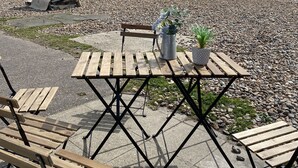 A beachside seating area with wooden tables and benches, a potted plant, and a boat in the background. - Beach 180: Beachfront Apartment, Sea views & Private Driveway Parking  (Worthing)