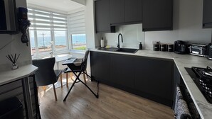 A modern kitchen with a large island, dark cabinetry, and a view of the sea. - Beach 180: Beachfront Apartment, Sea views & Private Driveway Parking  (Worthing)