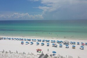 A beach with white sand, clear turquoise water, and numerous blue umbrellas.