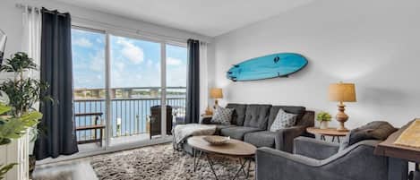 A living room with a sofa set, a coffee table, and a view of a body of water through large windows.
