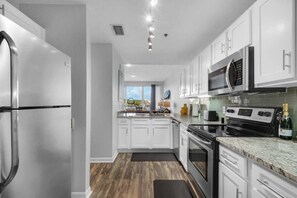 A modern kitchen with white cabinets, stainless steel appliances, and a wooden floor.