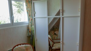 Ein Zimmer mit Holzboden, einem Sessel mit Blumenmuster, einem weißen Kleiderschrank und einem Fenster mit Vorhängen.