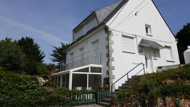 Ein weißes, zweistöckiges Haus mit Balkon, einer Veranda und einer Treppe, die zum Eingang führt.