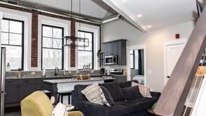 A modern kitchen with a central island, dark grey cabinets, and a large window. - Lake Lookout Penthouse Loft (Boyne City)