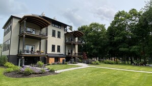 A two-story building with balconies, a covered outdoor seating area, and a well-maintained lawn. - Lake Lookout Penthouse Loft (Boyne City)
