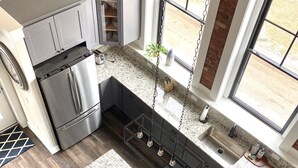 A modern kitchen with a central island, stainless steel appliances, and large windows. - Lake Lookout Penthouse Loft (Boyne City)
