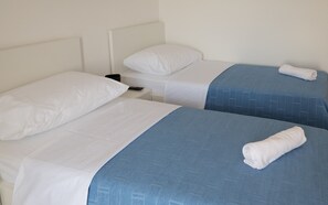 Two single beds with white linens and a blanket, a nightstand with a remote control.