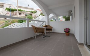 Relax on the balcony with two comfortable chairs and a small table, surrounded by a potted plant and a view of the city.