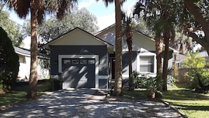Une maison d’habitation avec un garage, entourée de palmiers et d’une pelouse bien entretenue.
