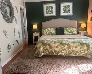 Une chambre à coucher comprenant un lit, deux lampes de chevet, une table de nuit, une porte et un mur orné de reproductions botaniques encadrées.