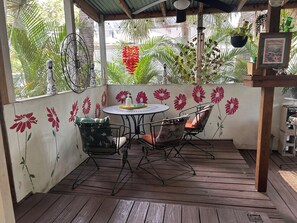 A covered patio with a round table and chairs, surrounded by a wooden deck and a wall with floral decorations.