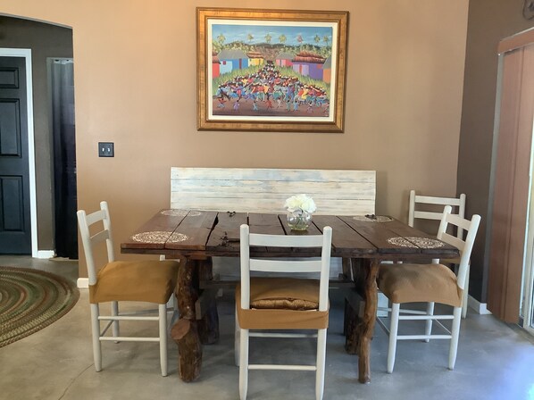 A dining area with a wooden table, white chairs, and a bench. A framed painting hangs on the wall above the table.