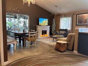 A living room with a fireplace, a dining area, and a large window with a view of greenery.