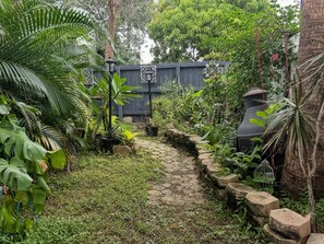 A garden pathway with a stone border, surrounded by various plants and trees.