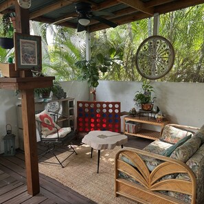 A covered outdoor seating area with a wooden ceiling, a round table, wicker furniture, and a wall-mounted decorative wheel.