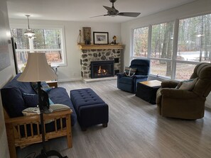 Ein Wohnzimmer mit Kamin aus Stein, einem blauen Sessel, einem braunen Sessel und einem Couchtisch aus Holz.
