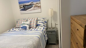 A bedroom with a bed, pillows, a nightstand, a lamp, and a wooden dresser. - Cozy cottage just one mile from the Platte river, close to the Sleepy Bear dunes (Honor)