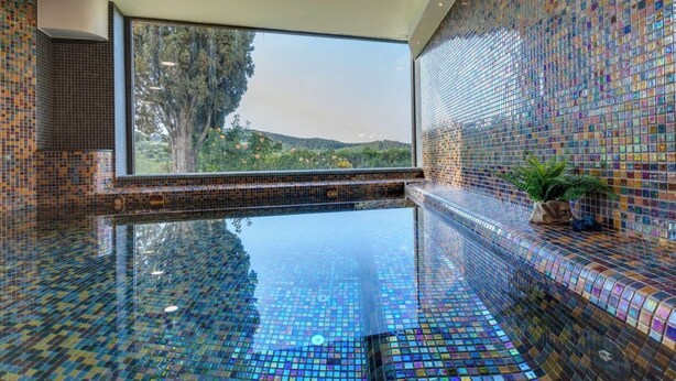 Una piscina infinita con paredes de mosaicos y un amplio ventanal con vistas a un paisaje natural.