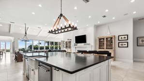 Una cocina moderna con una isla grande, armarios blancos y una lámpara de araña.