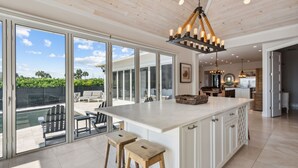 Una cocina amplia con una isla grande, armarios blancos y vista al jardín trasero.
