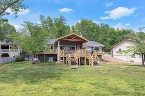 A two-story house with a wooden deck, a fenced yard, and a clear sky.