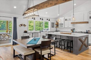A modern kitchen with a central island, wooden beams, pendant lighting, and large windows.