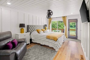A bedroom with a bed, a nightstand, a lamp, a sofa, and a TV.