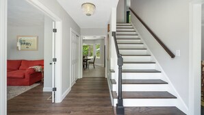 A staircase with wooden steps and a black handrail, leading to a dining area with a table and chairs. - Beautiful Colonial Home in Saunderstown, RI (North Kingstown)